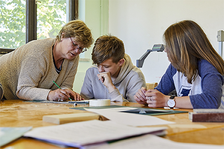 Das Foto zeigt eine Lehrerin mit zwei Schülern beim Zeichnen einer Schablone.